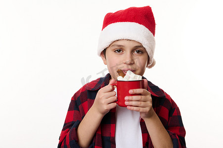 正电子摄影照片_快乐的多民族儿童男孩戴着圣诞老人的帽子，享受一杯美味的热可可和棉花糖。