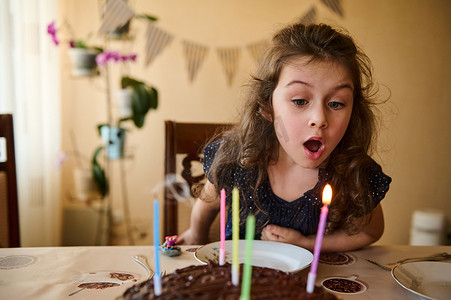 快乐的小女孩，长着漂亮的长卷发，穿着优雅的裙子，吹灭生日蛋糕上的蜡烛