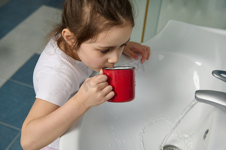 特写肖像小女孩穿着睡衣，在家庭浴室刷牙时用水冲洗嘴巴