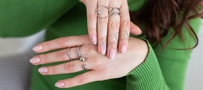 横幅特写女性手与时髦的浅粉色美甲佩戴时尚的戒指首饰。