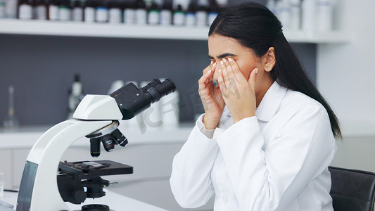 工作揉眼睛摄影照片_女科学家通过显微镜观察并在眼睛疲劳或不适时揉眼睛。