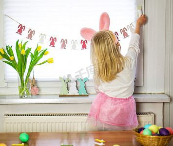 粉红色摇滚和白色衬衫的小女孩为复活节装饰房间。