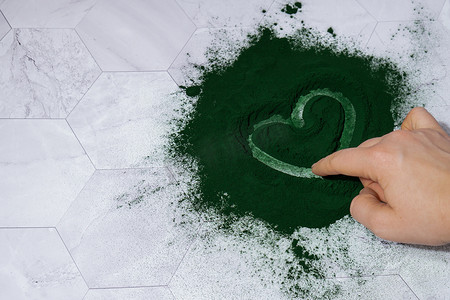 爱心手托卡通摄影照片_女手在蓝绿藻小球藻和螺旋藻粉上画心。