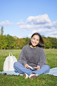 可爱少女的垂直照片坐在公园的草地上，背着背包和她的书，独自在户外读书