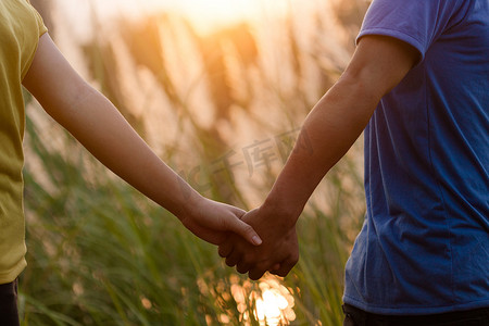 阳光下，相爱的年轻夫妇牵着手在公园散步