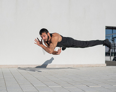 一名身穿黑色运动服的男子在户外做俯卧撑时跳跃。