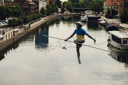 波兰比得哥什 - 2022 年 8 月，比得哥什的布尔达河男子穿越河流雕塑，一名男子在钢丝上保持平衡，旧粮仓建筑，库亚维-波美拉尼亚。
