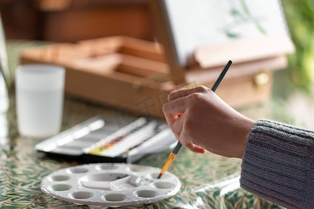 年轻的左撇子女孩在家里用调色板混合水彩颜料画静物画