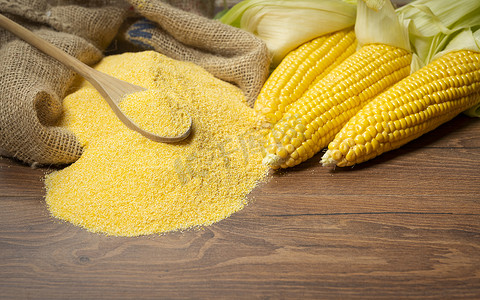 勺子黄色摄影照片_背景中成熟的年轻甜玉米芯勺和玉米粉
