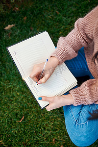 草地视频摄影照片_模糊的草地背景上拿着笔和纸日记的女性手