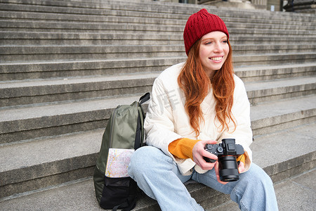 年轻的学生，摄影师坐在街边的楼梯上，用专业相机检查她的照片，在户外拍照