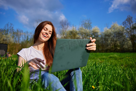 草地俯视图摄影照片_在高草地上度假时用笔记本电脑工作的快乐女人