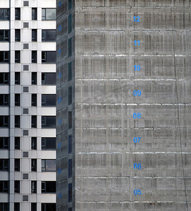 正在建设中的一栋高层公寓楼的混凝土核心筒，楼层编号用蓝色油漆标记，背景是高塔上的银色包层