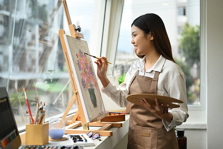 美丽的亚洲女性在画布上用丙烯酸颜料画画，享受创造性的休闲活动。