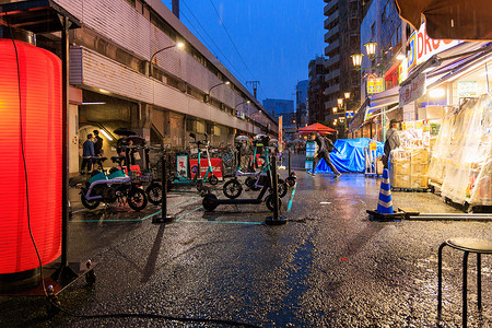 日本大阪 — 2023年4月29日：雨夜明亮的药店和火车站停放的电动摩托车和自行车