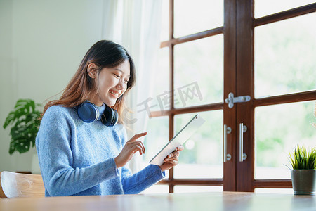 一位亚洲少女使用平板电脑、戴着耳机在图书馆的木桌上通过视频会议在线学习的肖像