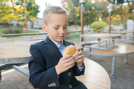 男孩小学生在户外咖啡馆吃汉堡、三明治。