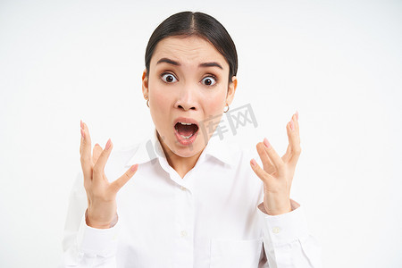 女脸手摄影照片_愤怒的办公室女士，亚洲女商人因愤怒而尖叫和握紧拳头，因沮丧而颤抖，站在白色背景上，发脾气