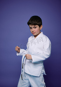 一个英俊的白人十几岁男孩的肖像，合气道摔跤手在紫色墙壁背景下练习武术。