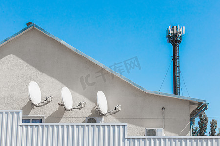 蓝天互联网塔背景下住宅楼墙上的卫星电视白盘天线信号与通信