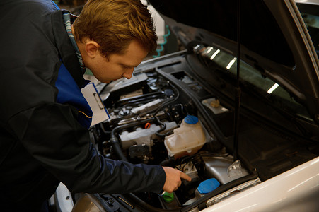 机械师在引擎盖下检查汽车的俯视图，在汽车维修车间检查发动机。