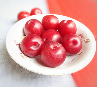 五颜六色的红李子放在红白背景的碗里，降低患癌症心脏病和糖尿病的风险
