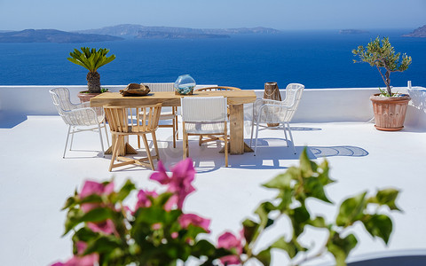 露台餐厅摄影照片_希腊圣托里尼海边一家餐厅的户外露台，海边的椅子和桌子上放着鲜花