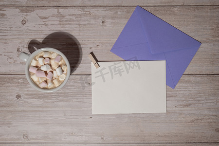 空的问候语或邀请卡模拟紫罗兰色信封，白色咖啡和棉花糖在木制蓝色背景上。