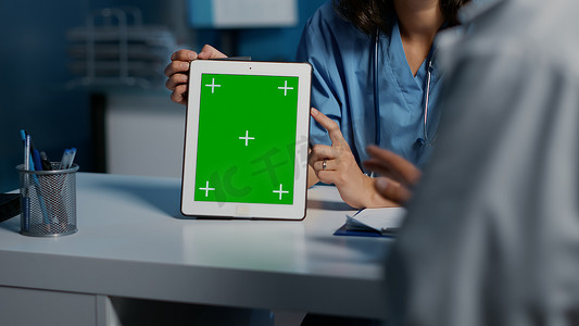 医院医生模板摄影照片_助理向医生展示带有绿屏模板的平板电脑
