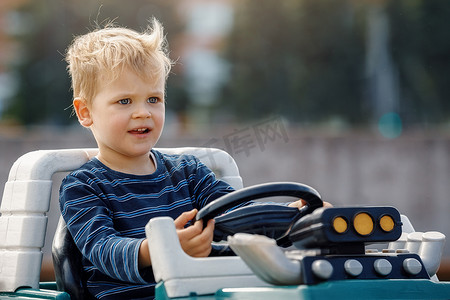 可爱的小男孩驾驶带方向盘的大型电动玩具车在户外玩得开心。