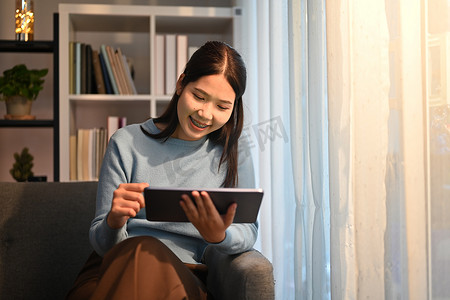 宜人的千禧一代女性坐在客厅里阅读电子邮件或在数字平板电脑上检查日常工作