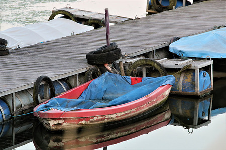 木码头上带蓝色防水油布的红色划船靴