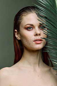 美女拿叶摄影照片_一位美丽、优雅的女士站在她的脸附近拿着一片棕榈叶，看着别处的美女肖像。
