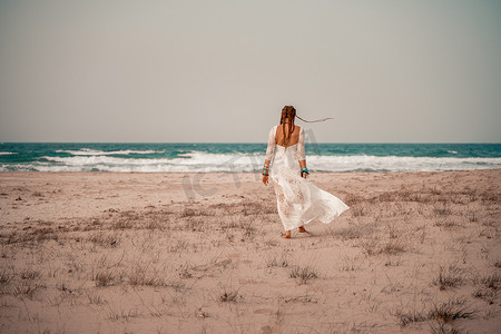 沙滩上的模特摄影照片_在沙滩上穿着白色长裙和银首饰的波西米亚风格模特。