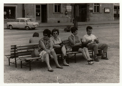 复古照片显示一群人坐在室外的长椅上，1960 年代。