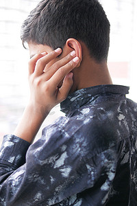疼痛摄影照片_十几岁的男孩耳朵疼，摸着他疼的耳朵，