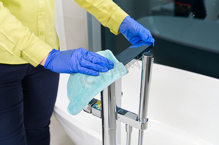 管家、家庭主妇或酒店女佣在浴室清洁独立式现代镀铬水龙头，特写