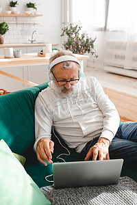 在家戴耳机在笔记本电脑上听音乐的老年老人画像 — 活跃的老年人概念