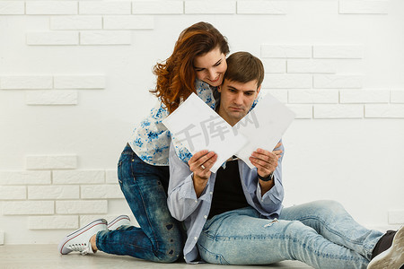坐着的会计摄影照片_微笑的夫妻坐着处理水电费和房屋维修文件，快乐的年轻夫妇阅读文书工作