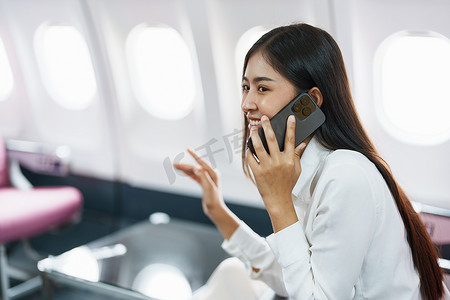 豪华飞机摄影照片_亚洲商务女性乘客坐在商务舱豪华飞机上，同时使用智能手机移动通话或视频会议和旅游概念工作