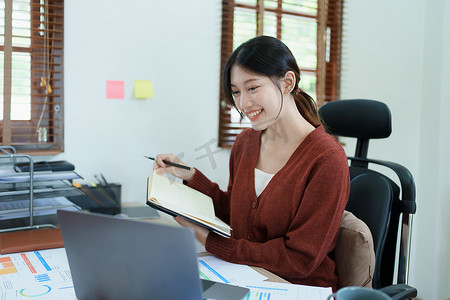 一位体贴的亚洲女商人的肖像，她正在查看财务报表并使用办公桌上的电脑和笔记本制定营销计划
