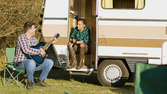 男朋友在复古露营车前用吉他唱歌