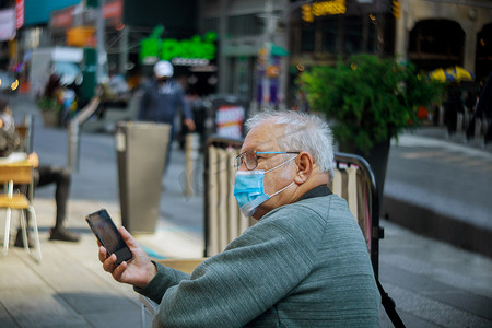 在纽约市使用手机的老人戴着面罩，以防止 covid-19 流感病毒新常态、大流行。