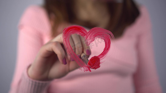 一位年轻女子在玻璃上画了一颗心。