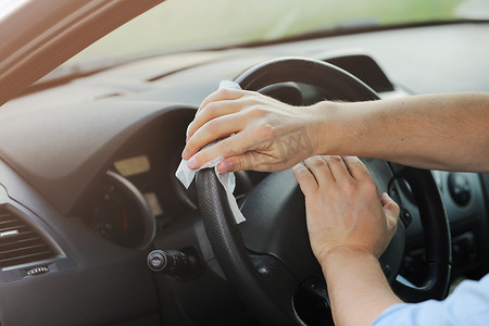 司机服务摄影照片_司机使用湿巾对汽车方向盘进行病毒或电晕病毒病消毒。