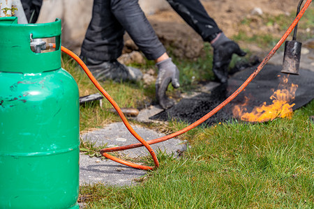 煤气罐摄影照片_借助煤气罐和明火为房屋地基防水的加热沥青带