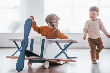 两个穿着复古飞行员制服的小男孩在室内玩玩具飞机