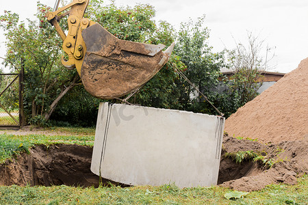 带桶的挖掘机，降低到钢缆混凝土下水道环上的坑中。