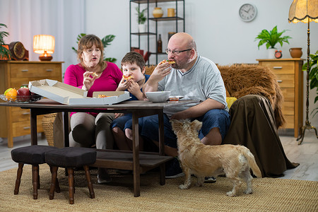 这家人给全家人分发披萨片，狗等着轮到它。