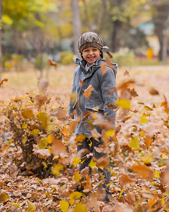 灰色外套摄影照片_穿着灰色外套和贝雷帽的白人男孩在秋天的森林里。